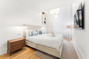 A modern bedroom with a bed, bedside tables, a nightstand, a large window with sheer curtains, and a wall-mounted TV. - Unique Luxury and Quiet in Porto’s Best Location (Porto)