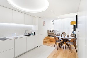 A modern kitchen with white cabinetry, a dining area with a wooden table and chairs, and a living room with a sofa and a lamp. - Unique Luxury and Quiet in Porto’s Best Location (Porto)
