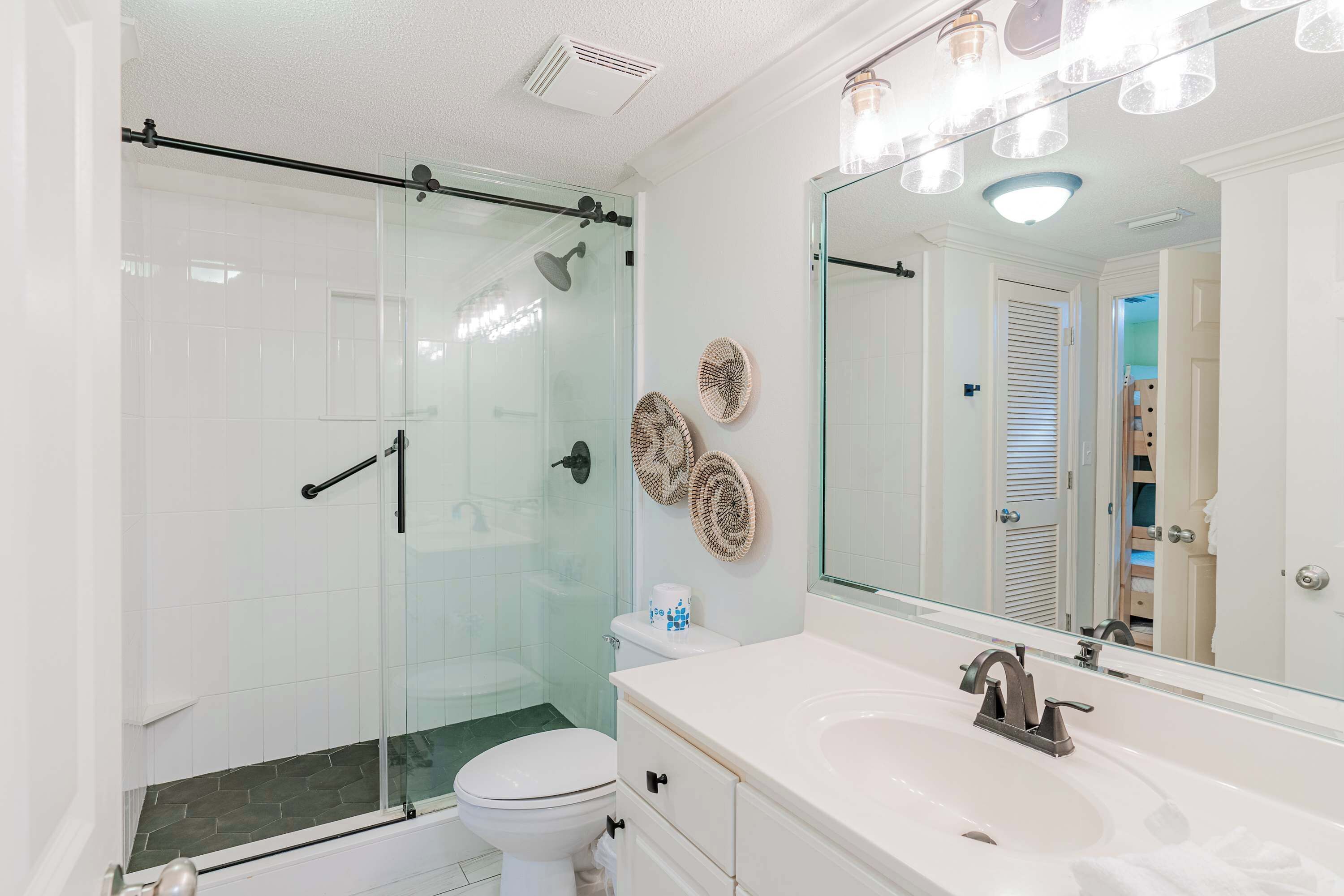 A modern bathroom with a glass-enclosed shower, a white toilet, a vanity with a sink, and a large mirror.