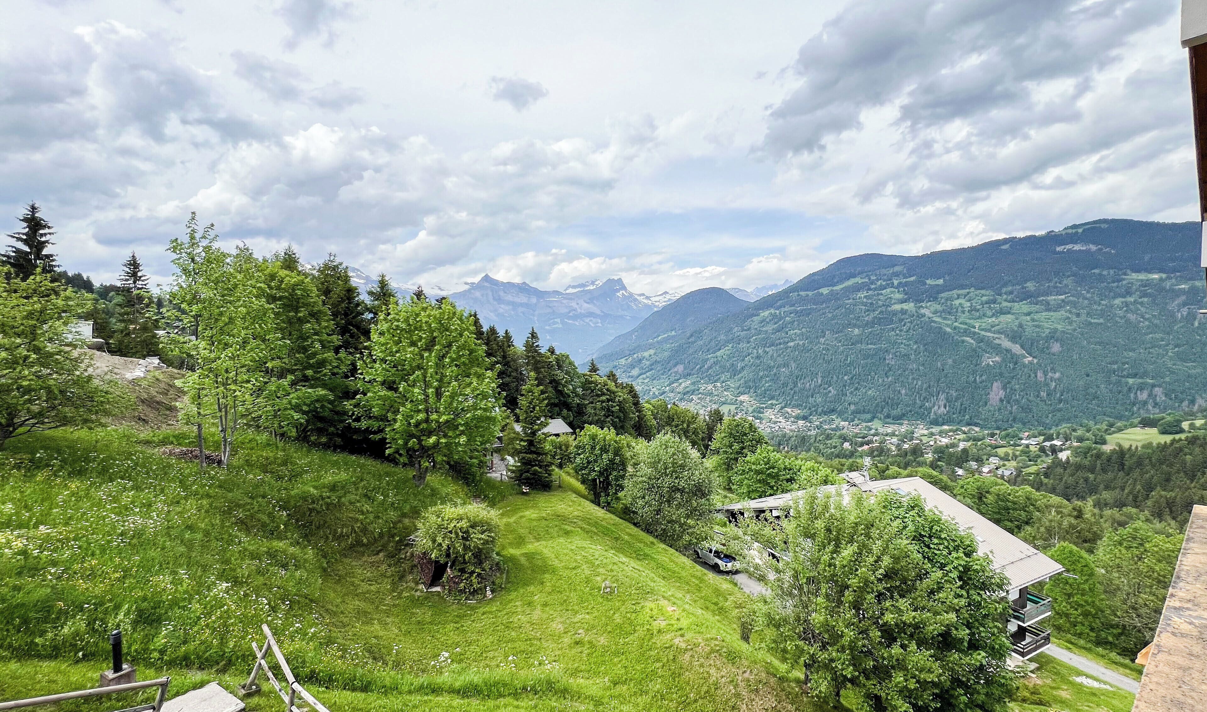 Une colline qui offre une vue sur une vallée et des montagnes. On y trouve des arbres et un petit bâtiment.