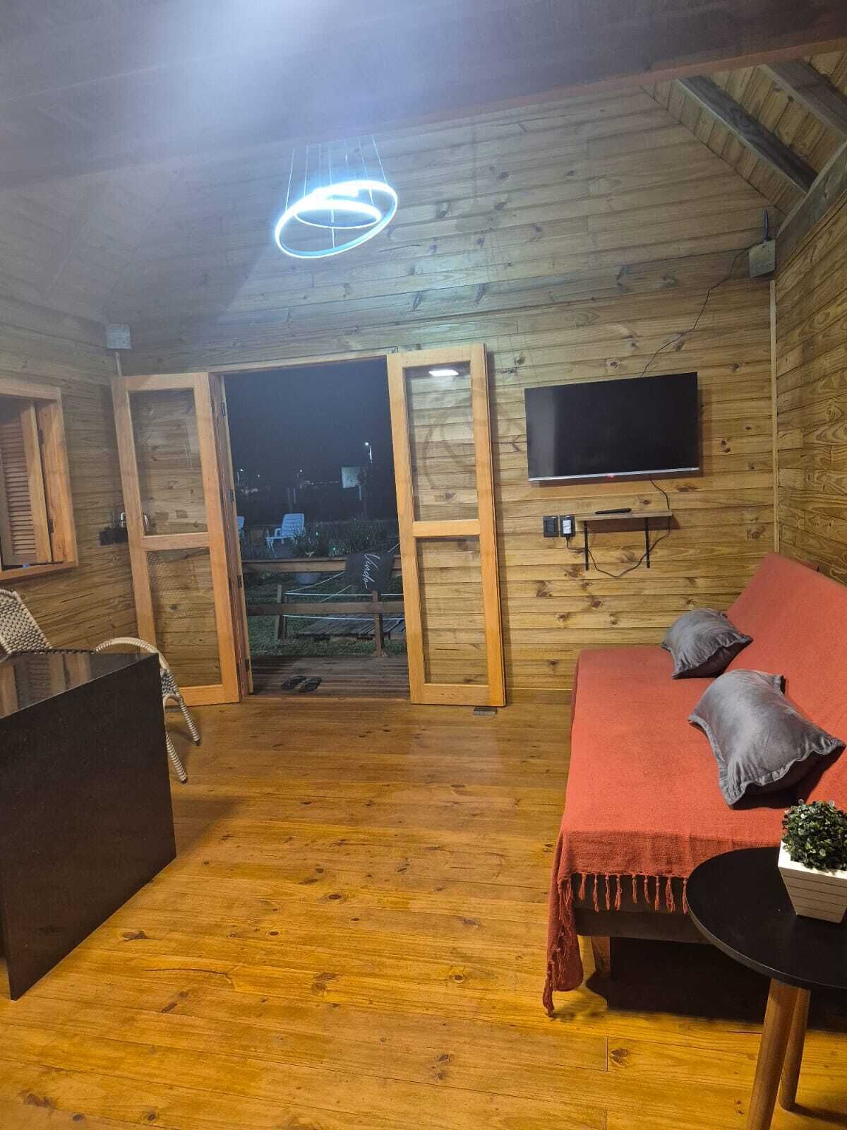 Una habitación acogedora de madera con un sofá rojo, una mesita con una planta y un televisor montado en la pared.