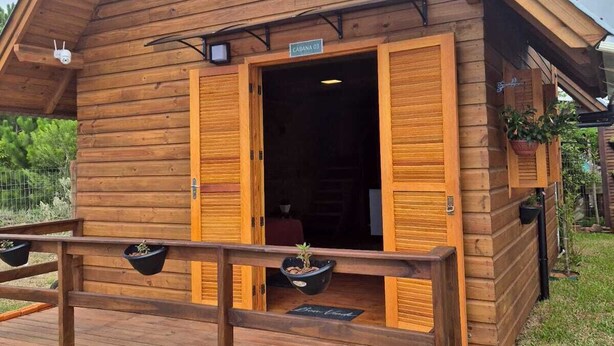 A wooden cabin with a sloped roof, an open entrance, and a wooden deck with planters. - Cabins in Torres, RS, offering leisure and relaxation in a cozy and peaceful location. (Torres)