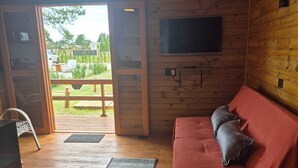 A cozy cabin interior with a wooden floor, a red sofa, a small table with a plant, and a TV mounted on the wall. - Cabins in Torres, RS, offering leisure and relaxation in a cozy and peaceful location. (Torres)