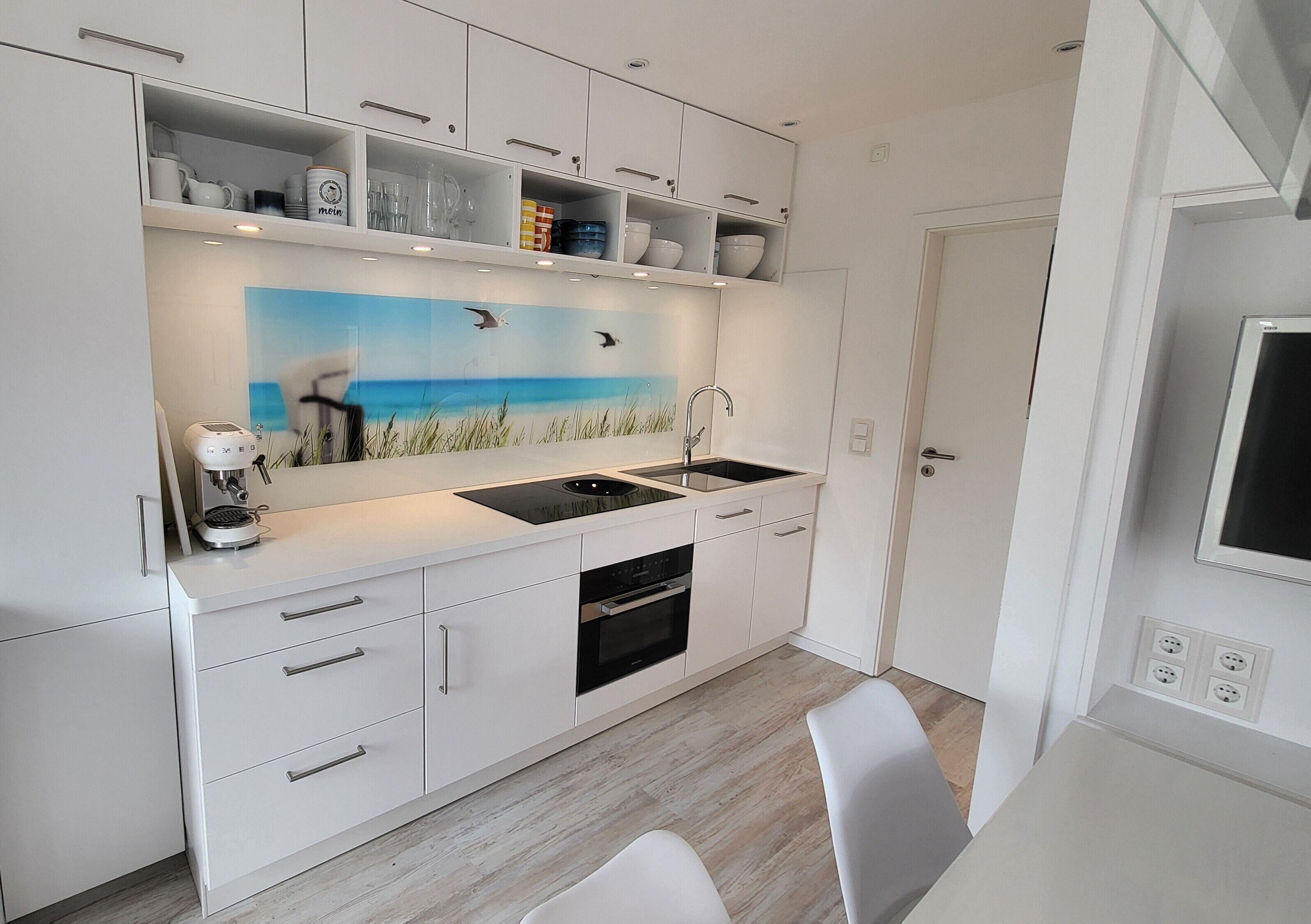 A modern kitchen with white cabinetry, a built-in oven, a sink, and a painting of a beach scene.