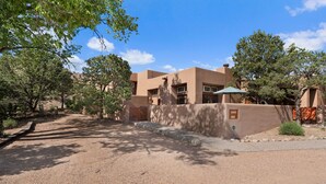 A desert-style building with a gravel driveway and surrounding trees. - Casa Golondrinas-A Serene Santa Fe Retreat (Santa Fe)