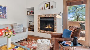 A living room with a fireplace, a sofa, a coffee table with a vase of flowers, and a view through a glass door. - Casa Golondrinas-A Serene Santa Fe Retreat (Santa Fe)