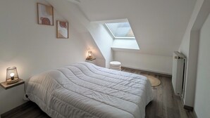Et soveværelse med skråvæg, ovenlys, en seng med hvid dyne, en sengetavlelampe og et lille natbord.