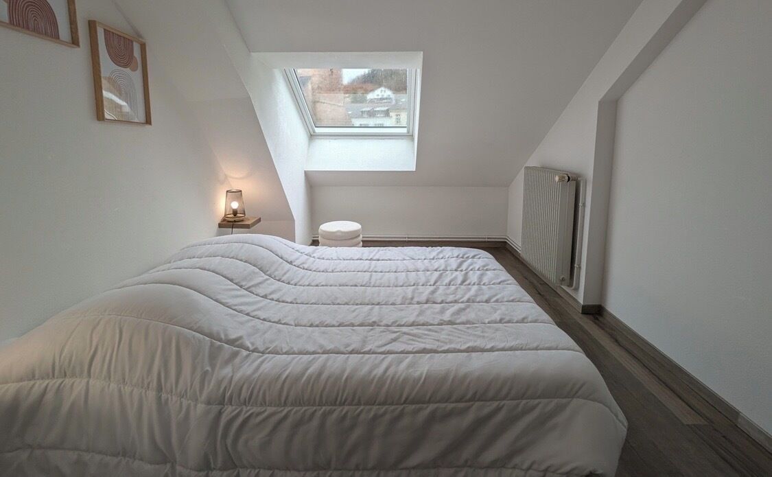 Un dormitorio con una cama grande, un tragaluz, un radiador y una mesita de noche con una lámpara.