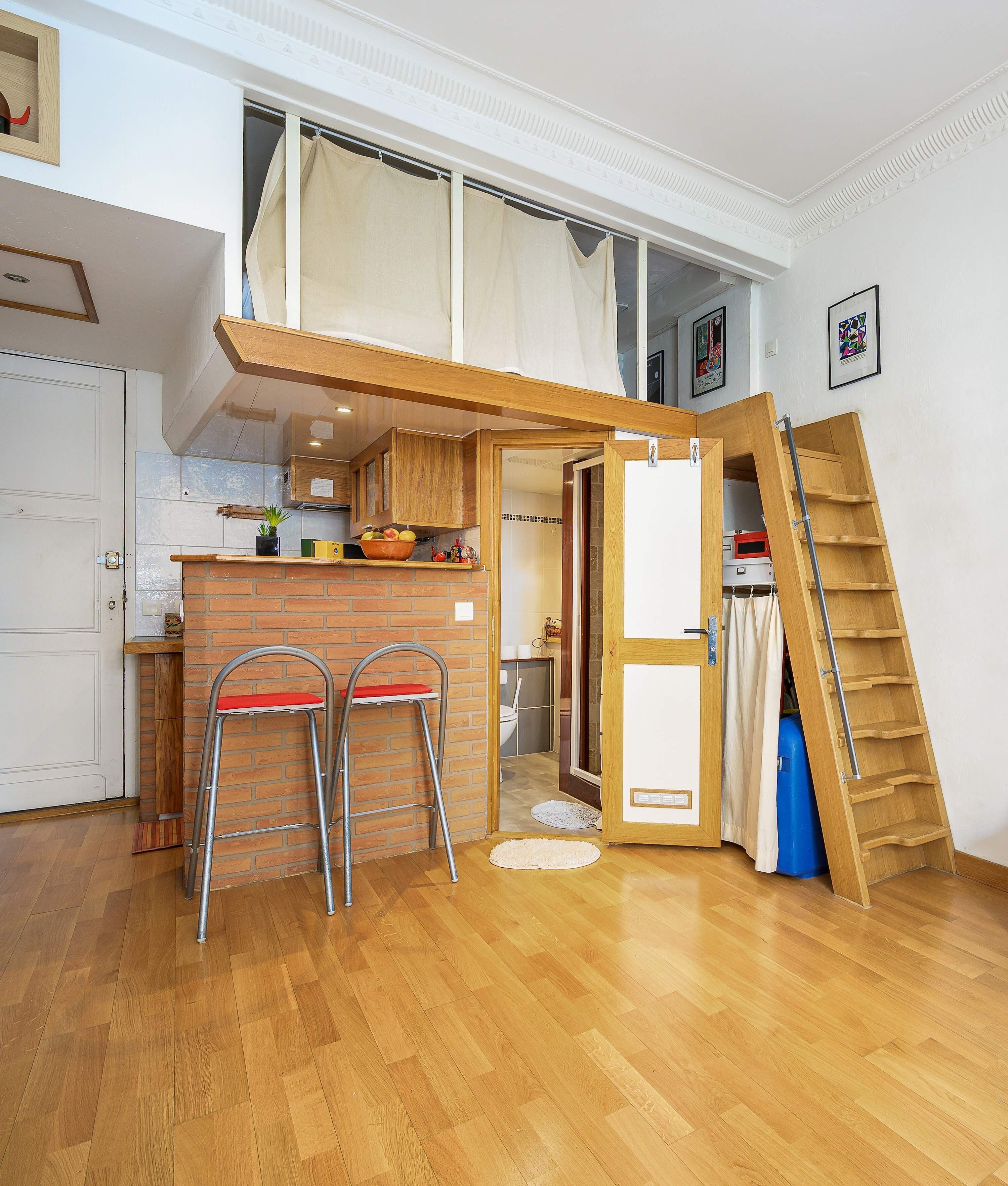 Una cocina compacta con mostrador de madera, dos taburetes y una pequeña mesa de comedor.