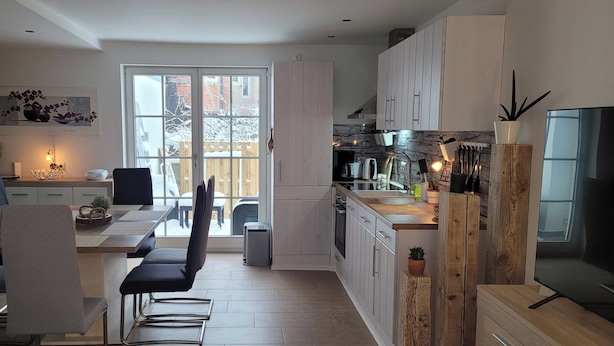 Una cocina moderna con armarios blancos, un comedor con mesa y sillas, y un ventanal que ofrece vistas al exterior.
