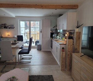 A modern kitchen with white cabinets, a dining area with a table and chairs, and a large window providing a view of the outside. - Modern "Stadtperle" vacation home in a great location! Plenty of space with a terrace!   (Bad Sülze)
