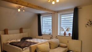 Un dormitorio con una cama, un sofá, una mesita y dos ventanas con persianas.