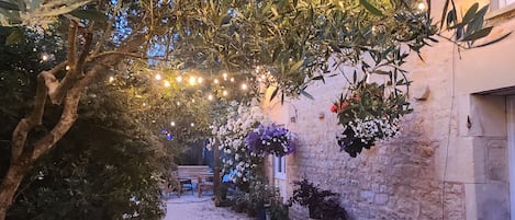 A courtyard with a gravel path, a stone wall, and hanging flower baskets.