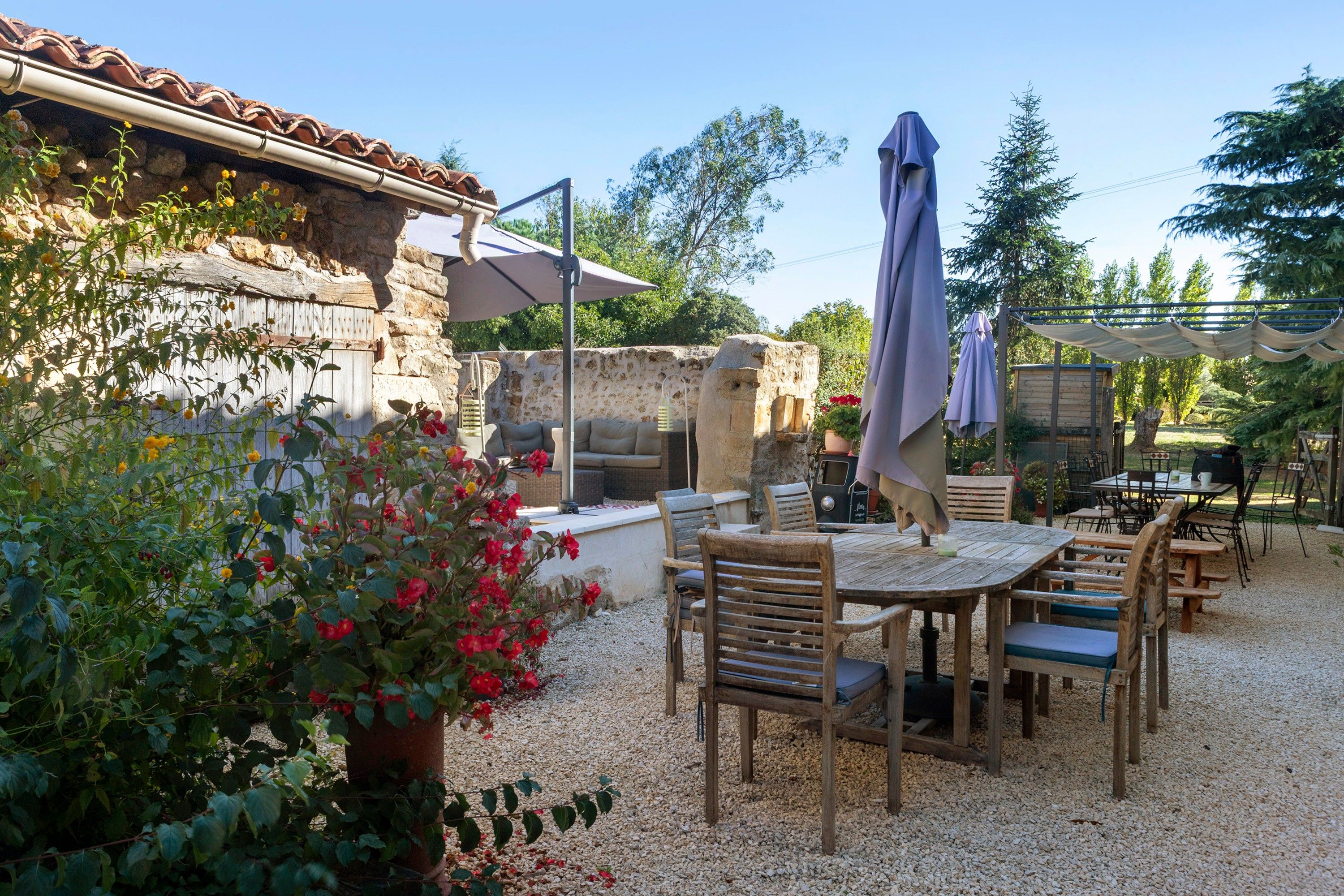 Un espace extérieur aménagé en terrasse, avec un mur en pierre, des meubles en bois et un sol recouvert de gravier.