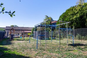 Ein Spielplatz mit Klettergerüsten und einer Rutsche, umgeben von einem Zaun und Bäumen.