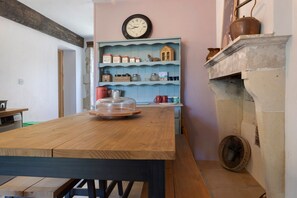 A kitchen with a wooden table, a clock, and a blue shelf with kitchenware.