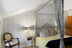 A four-poster canopy bed with a headboard, a bedside table with a lamp, and a chair.