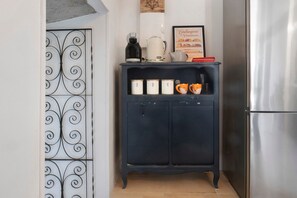 A kitchen with a dark blue cabinet, a coffee maker, and a framed menu on the wall.