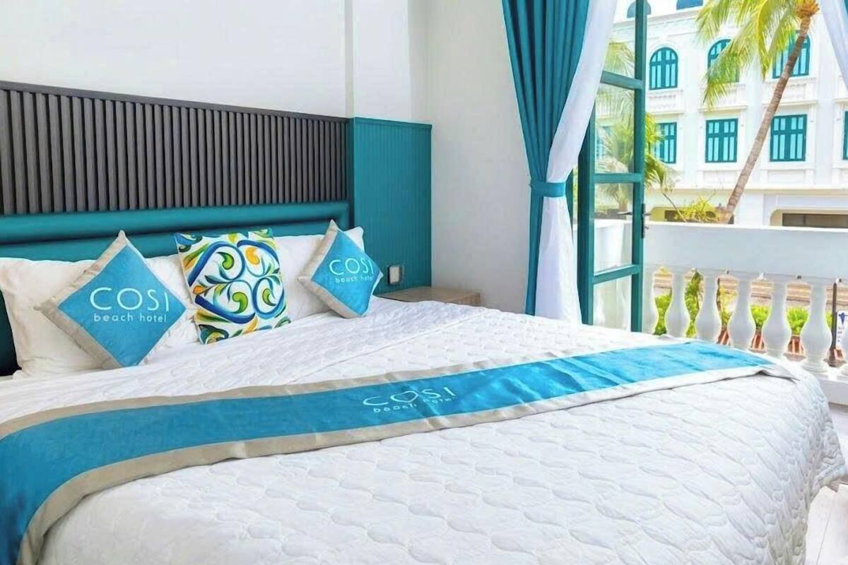 Une chambre d’hôtel avec un lit, une tête de lit et une vue sur un immeuble avec des fenêtres.