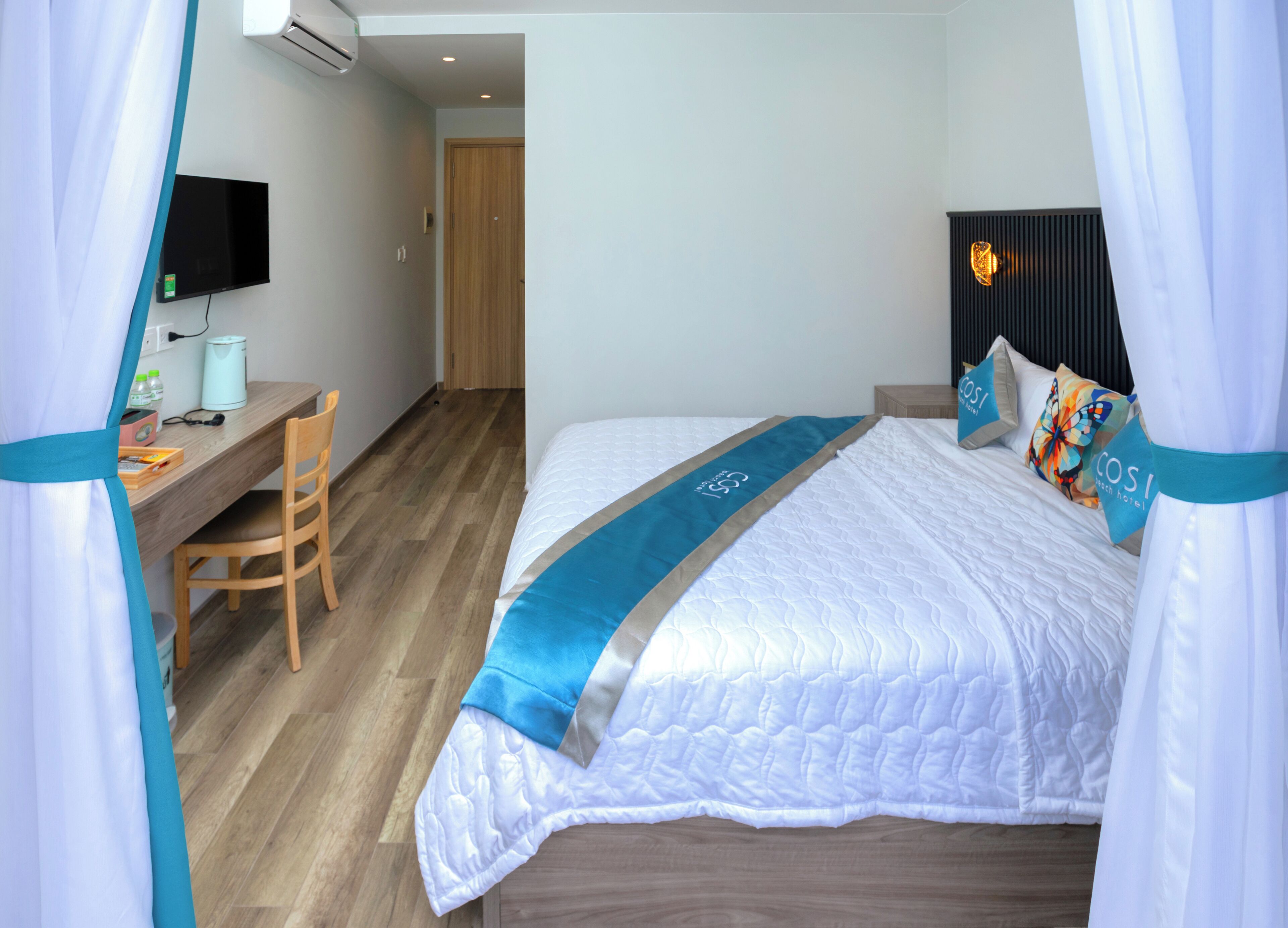 A hotel room with a bed, a desk, a chair, a television, and a door.