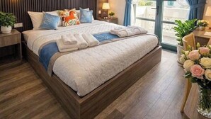 Une chambre d’hôtel moderne avec un grand lit, une tête de lit en bois, des lampes de chevet, une table de chevet, une fenêtre avec des rideaux et une vue sur la ville.