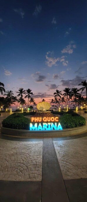 A sign with "PHU QUOC MARINA" illuminated in neon lights, surrounded by palm trees and a paved walkway. - Cosi Beach Hotel Phu Quoc (Phu Quoc)