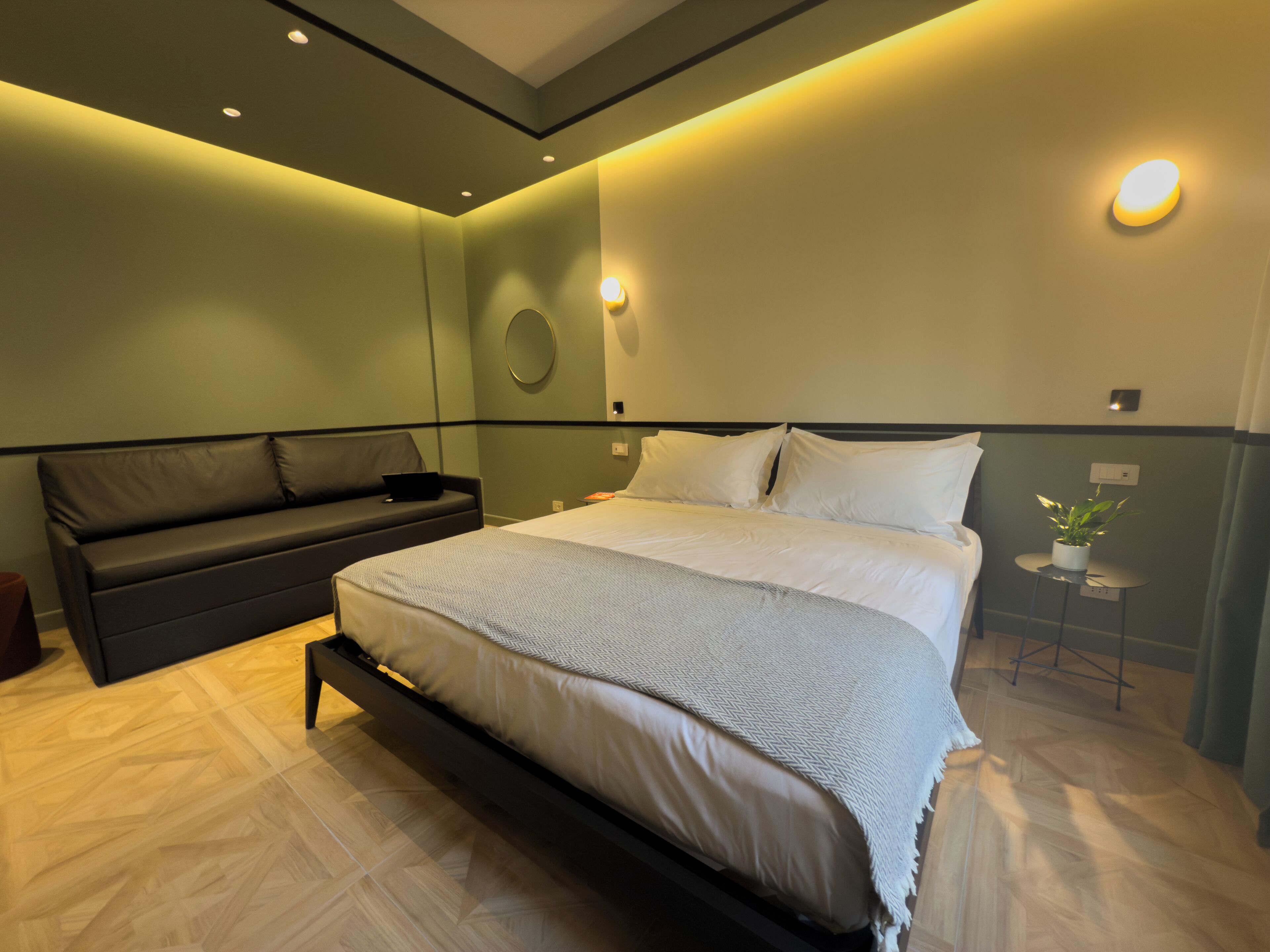 A modern bedroom with a large bed, a dark sofa, and a small table with a plant.