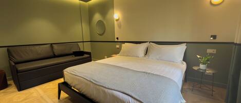 A modern bedroom with a large bed, a dark sofa, and a small table with a plant.