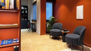 Ein modernes Wohnzimmer mit Bücherregal, zwei grauen Sesseln, einem kleinen Tisch und einer Topfpflanze.