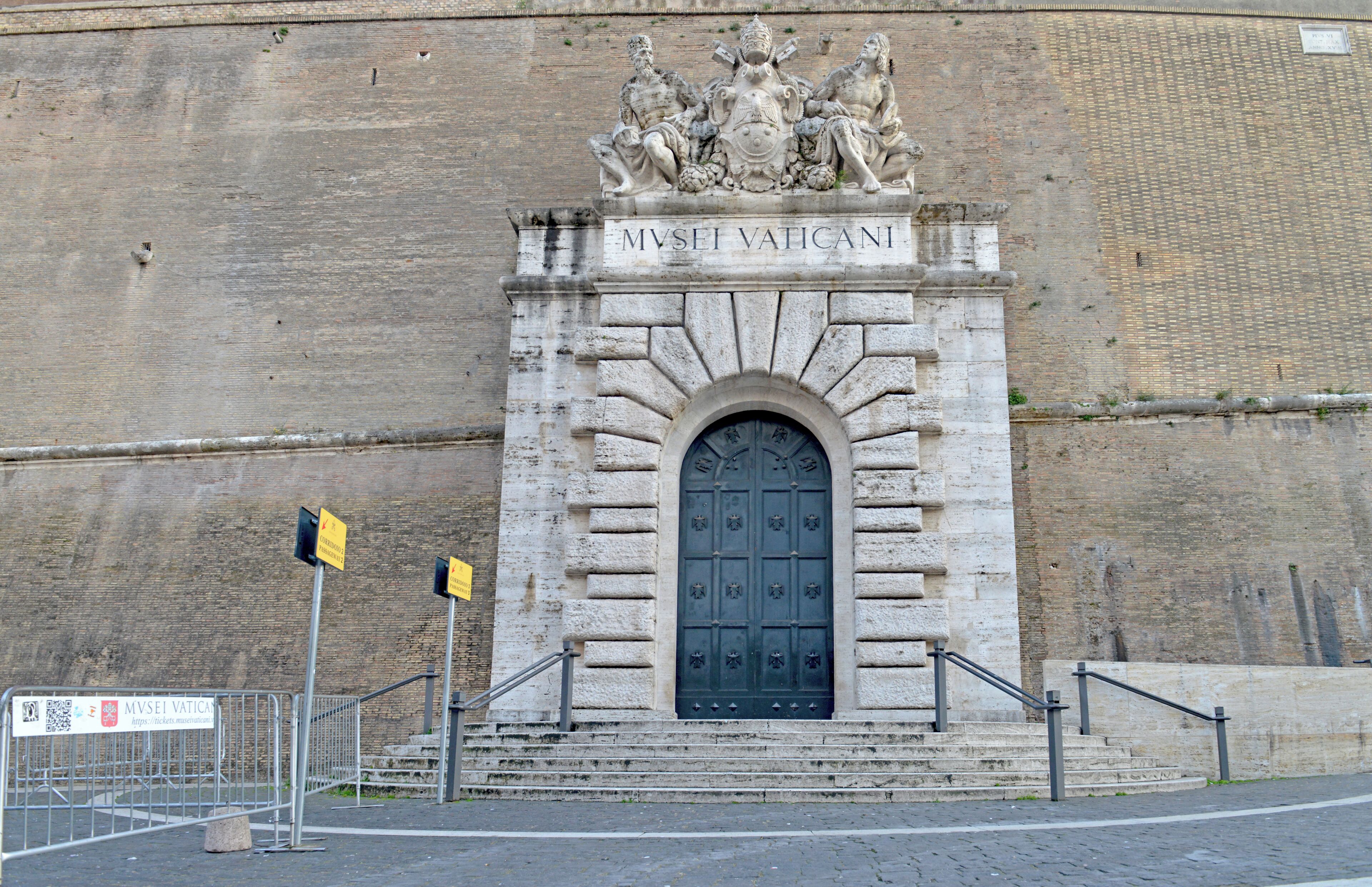 A stone entrance with a dark door, steps, and a metal railing.