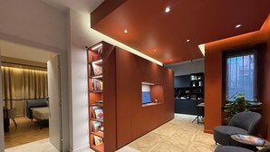 Eine moderne Hotelhalle mit einer großen Bücherwand, einer Sitzecke mit Stühlen und Blick zur Küche im Hintergrund.