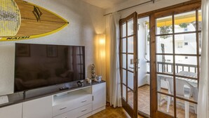 Una habitación con televisor de pantalla plana, ventilador de techo, puerta corredera de vidrio a un patio al aire libre y pared blanca.
