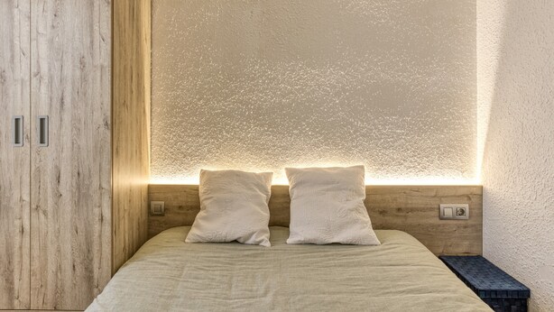 Un dormitorio con un armario de madera, una cama con dos almohadas y una pared con textura.