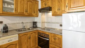 Een keuken met houten kastjes, een Bosch vaatwasser, een koffiezetapparaat en een koelkast.