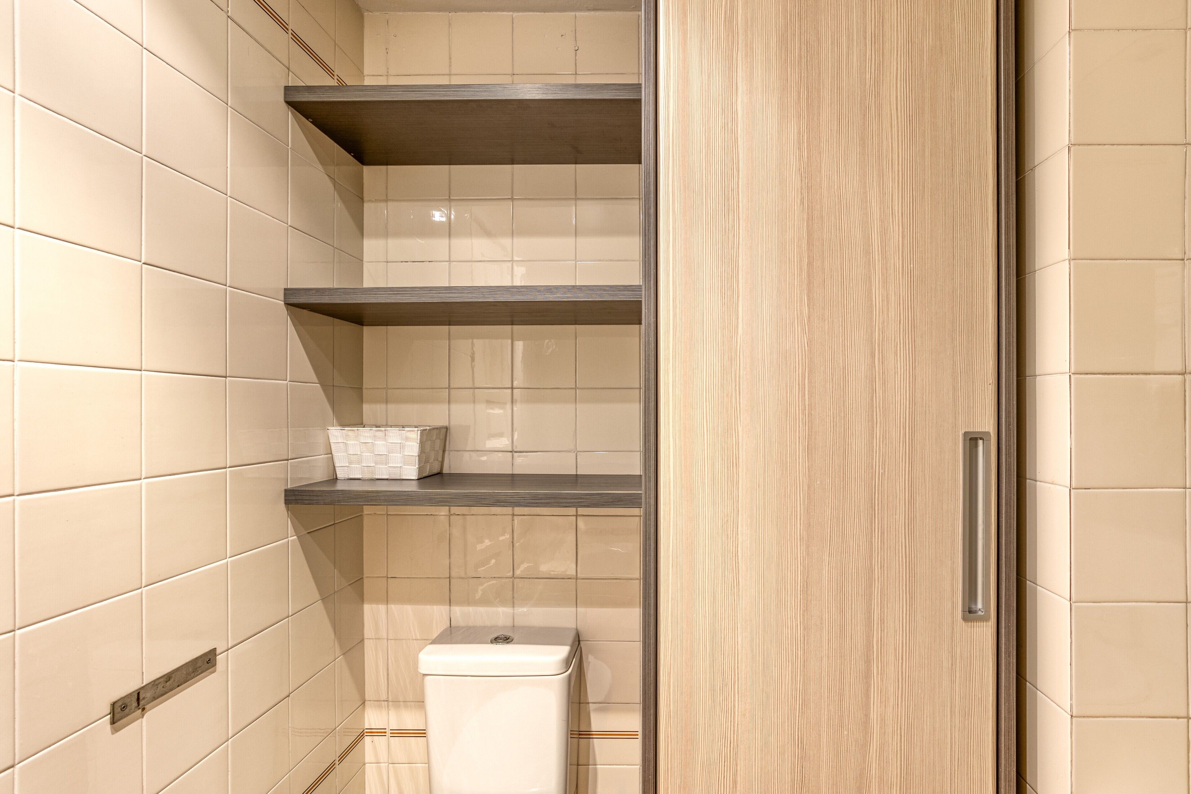 Un baño con paredes de baldosas color beige, un inodoro blanco y una puerta de madera con picaporte.