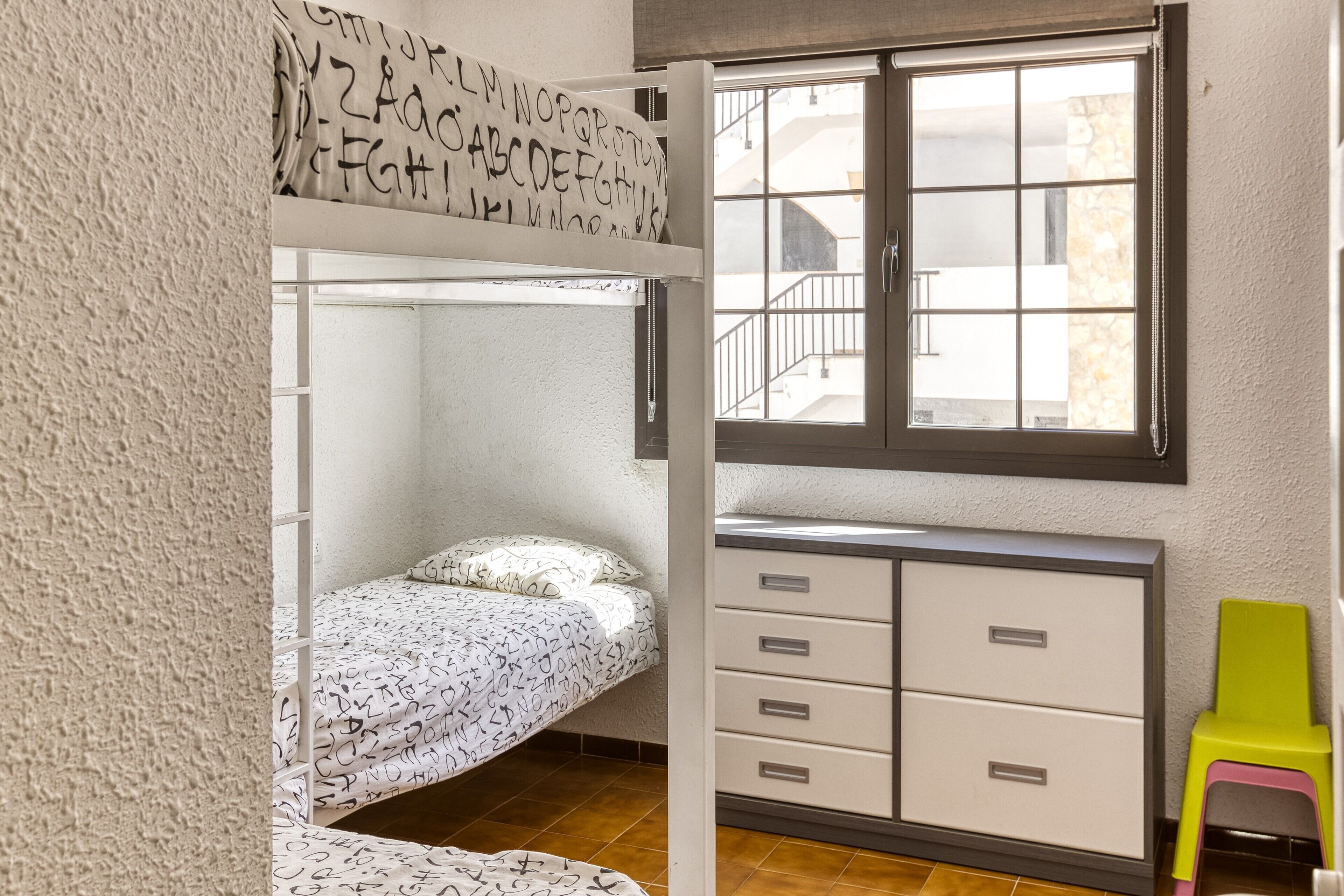 Una litera con ventana arriba, un escritorio con cajones y una silla pequeña.