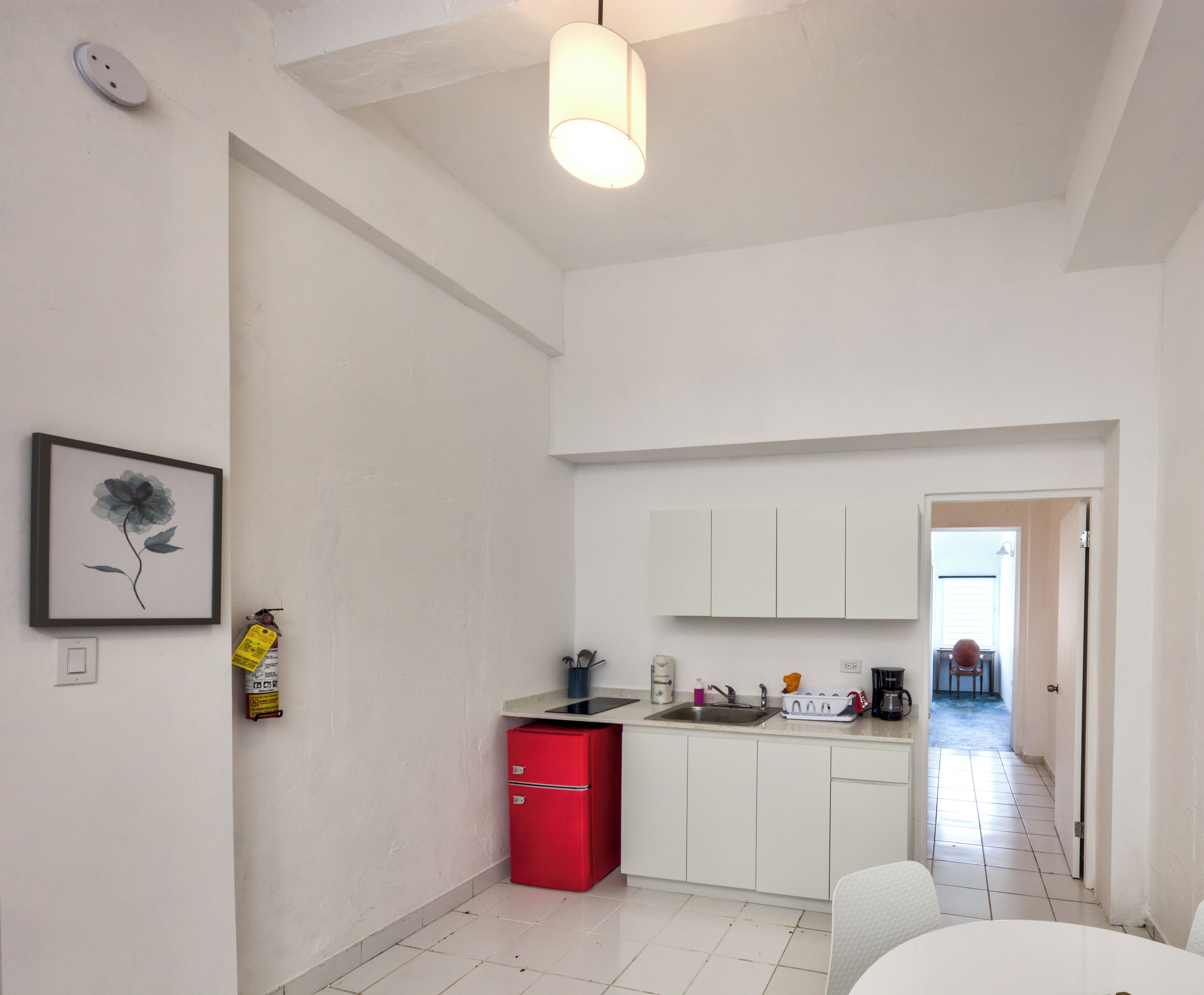 A compact kitchen with white cabinets, a red refrigerator, and a hanging light fixture.