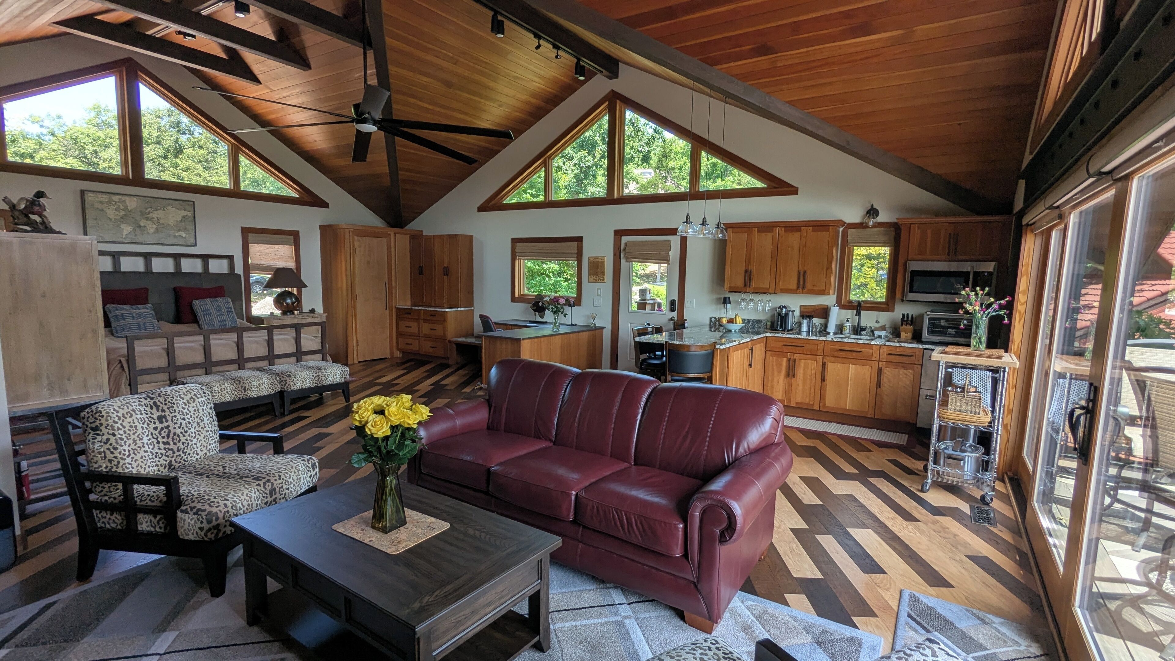 Un vaste espace de vie comprenant un canapé en cuir rouge, une table basse en bois et un fauteuil à motifs léopard. On peut également apercevoir une cuisine avec des meubles en bois et un coin repas avec une table et des chaises.