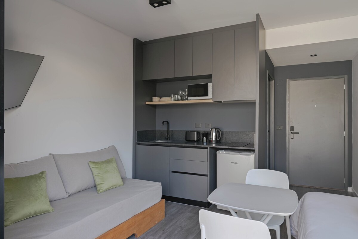 A compact kitchenette with a microwave, kettle, and small refrigerator. There is a sofa with cushions and a small table with chairs.