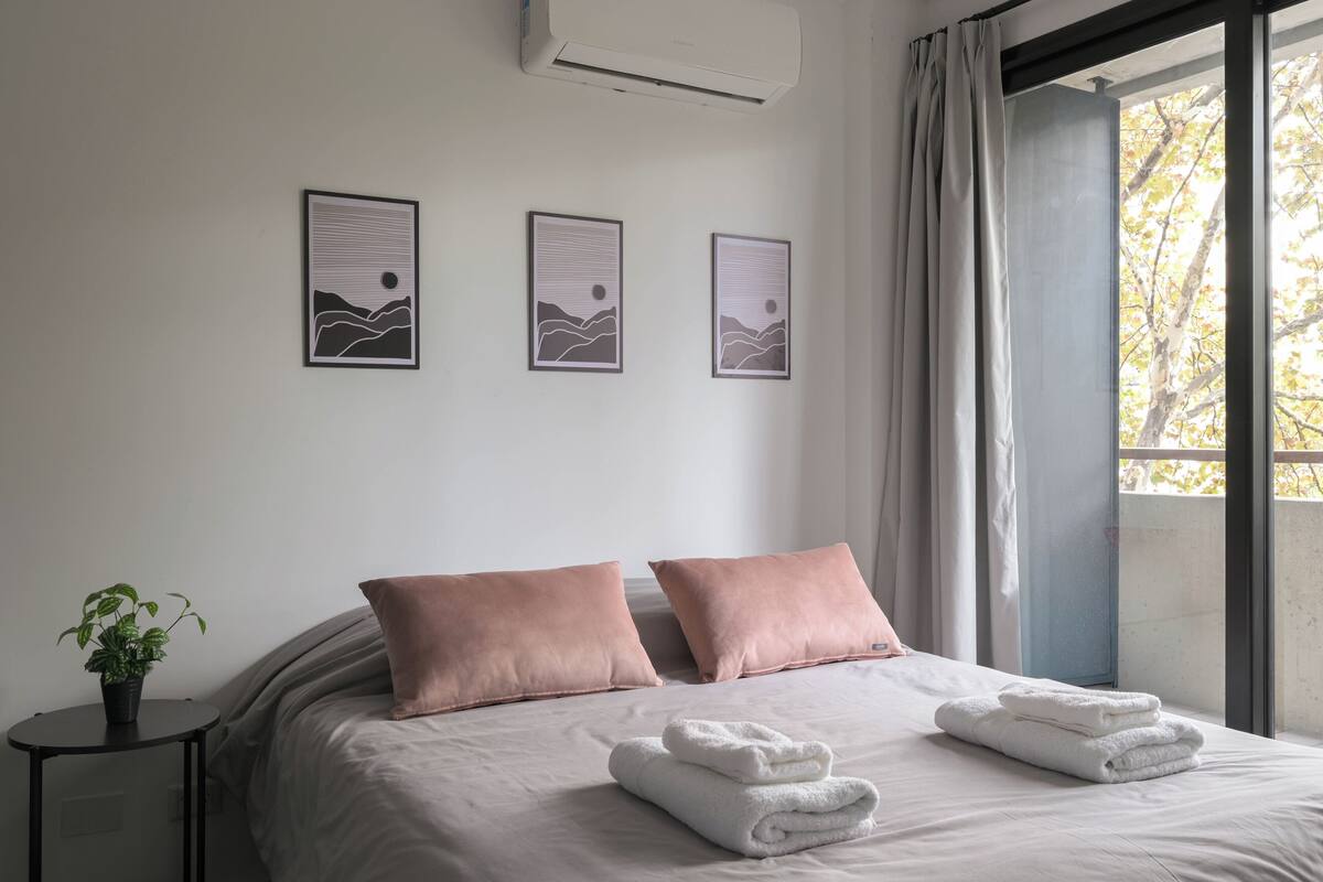 A bed with two pillows, a window with curtains, and three framed pictures on the wall.