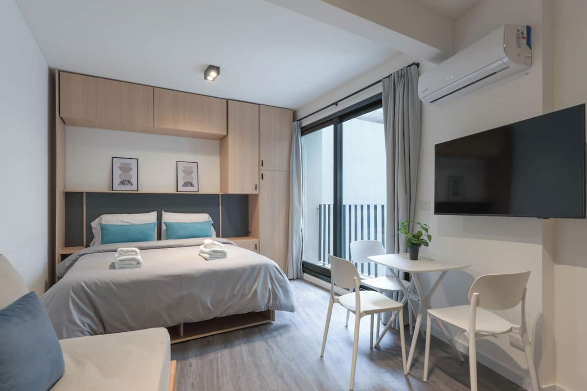 A modern hotel room with a bed, bedside tables, a TV, and a balcony with curtains.