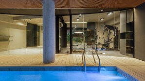 A modern indoor pool area with a wooden deck, a large pillar, and exercise equipment. - MOT Design SohoHaus (Buenos Aires)