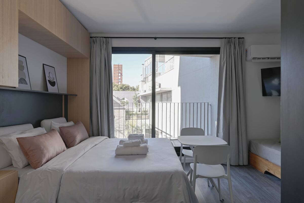 A modern hotel room with a bed, bedside table, and a view of the city.