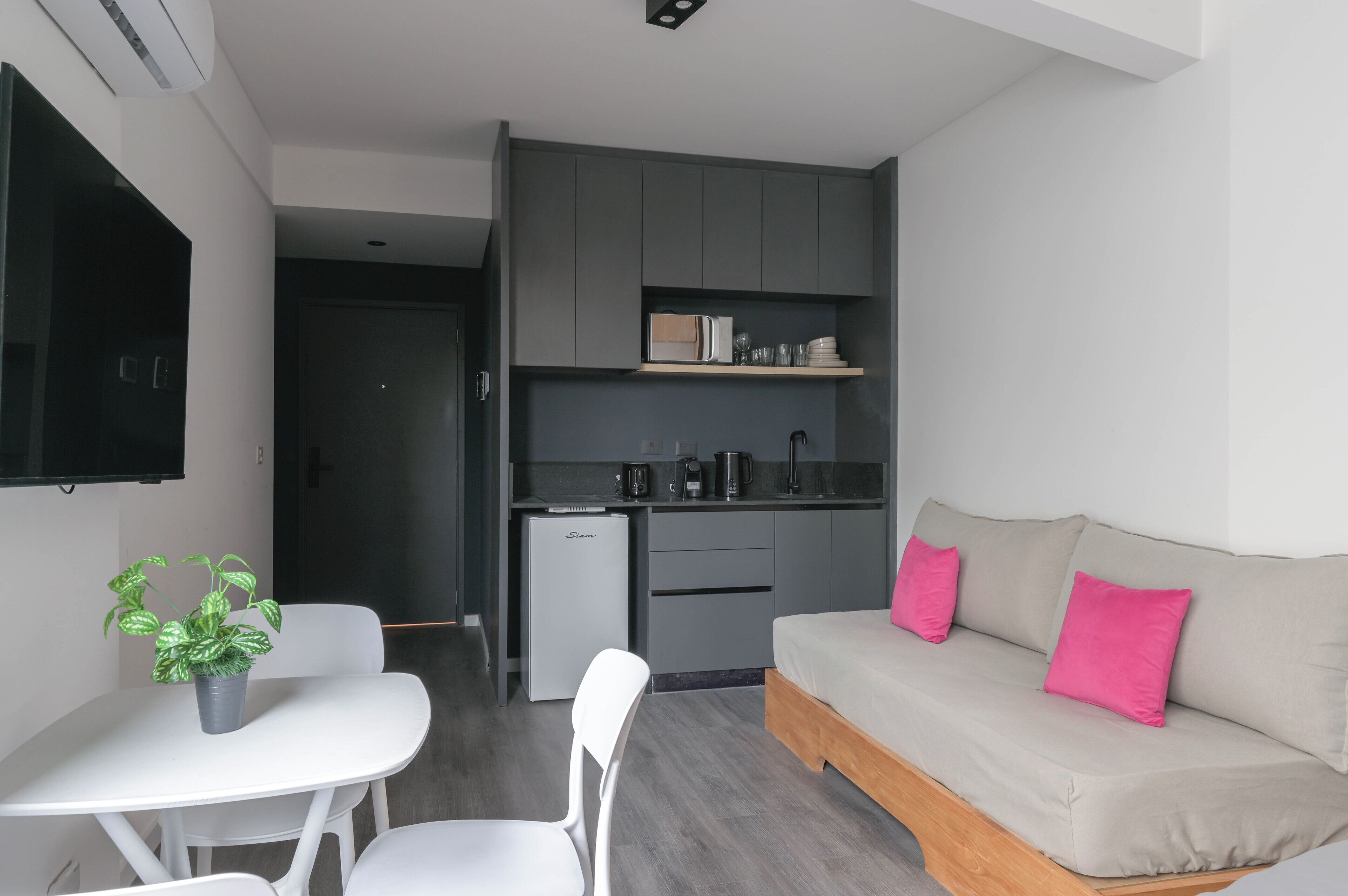 A compact living space with a kitchenette, a dining area with a table and chairs, a sofa with cushions, and a small refrigerator.