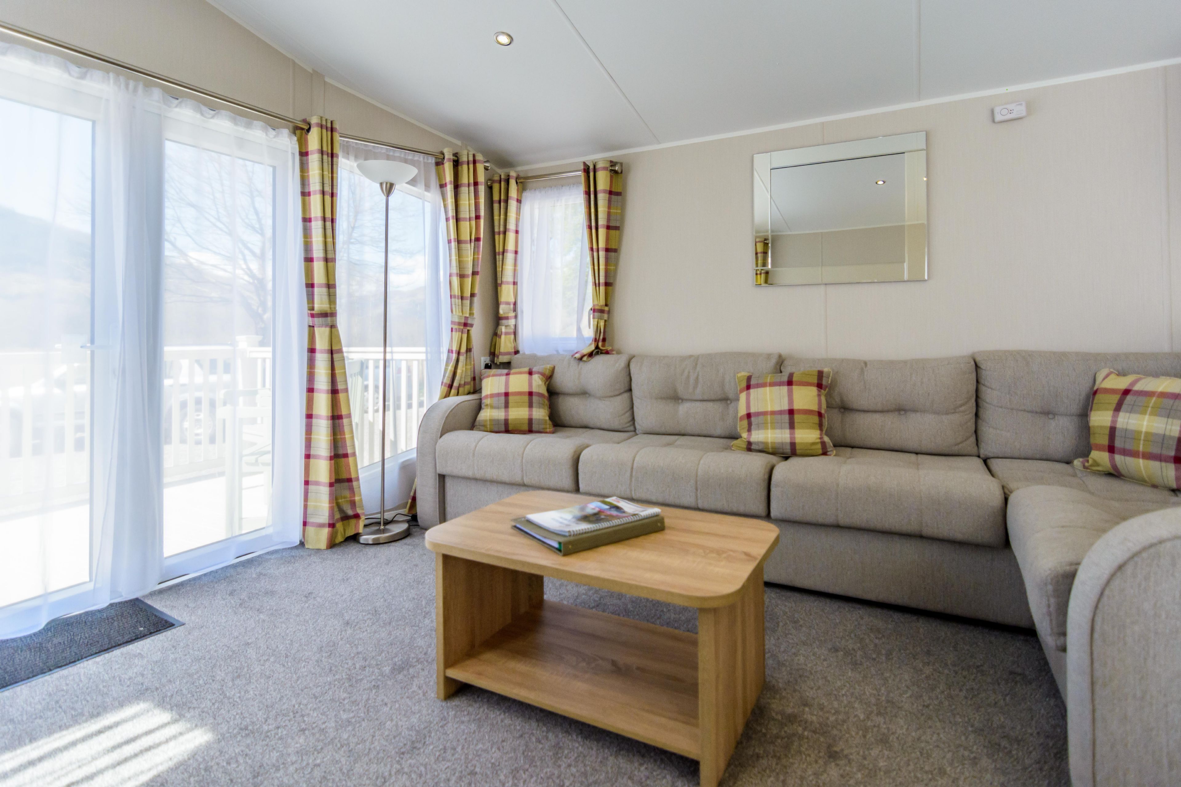 A living room with a beige sofa, plaid curtains, a wooden coffee table, and a large window.