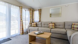 En stue med en beige sofa, ternede gardiner, et træbord og et stort vindue.
