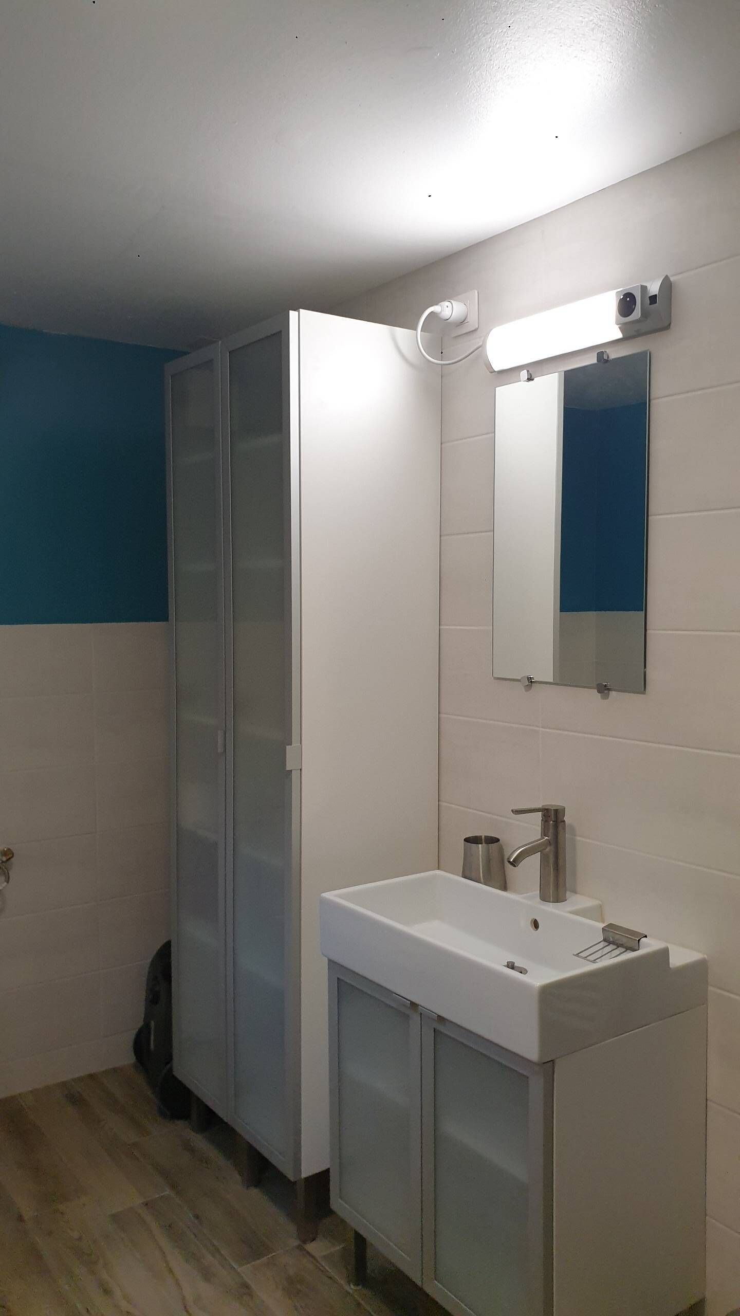 Casa de banho com lavatório branco, espelho e cabine de duche.