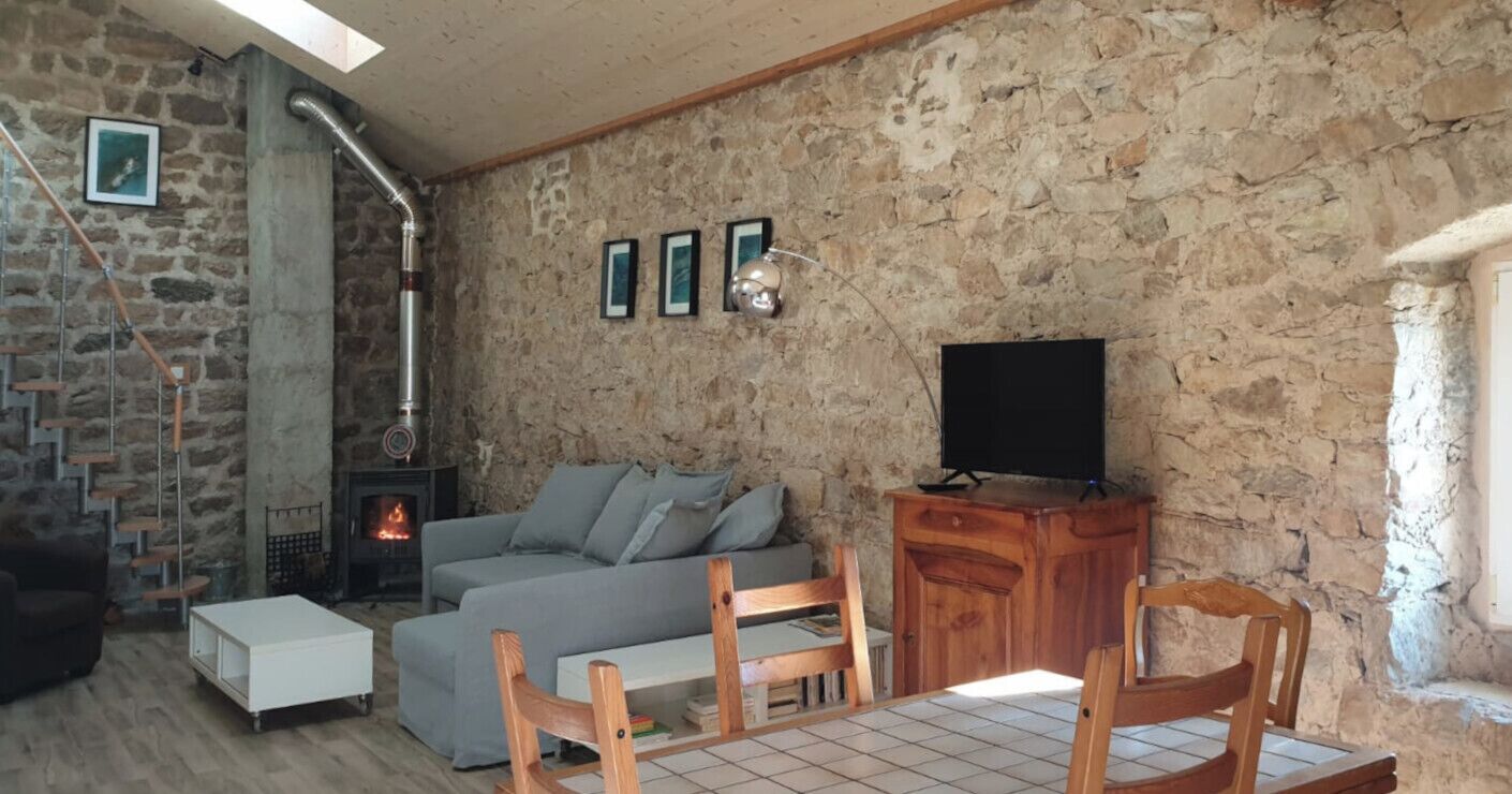 Un salon chaleureux avec un mur en pierre, une cheminée, un canapé, un téléviseur et des meubles en bois.