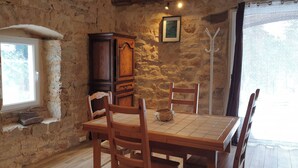 A rustic dining area with a stone wall, wooden table, chairs, and a cabinet. - A haven of peace in Rochepaule, in the heart of Ardèche verte (Rochepaule)