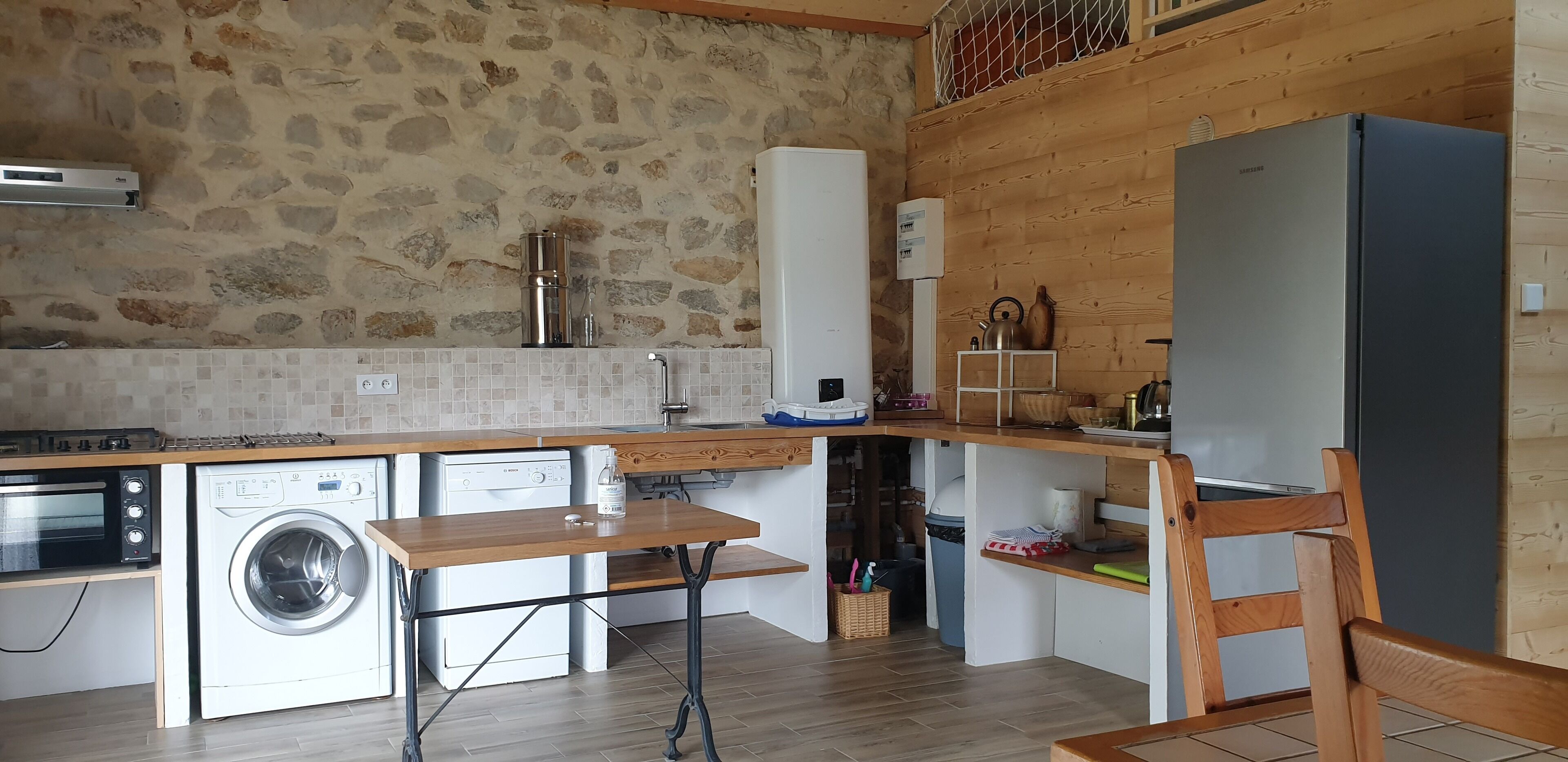 Eine kompakte Küche mit Steinwand, einer Waschmaschine, einem Einbauofen und einem Essbereich aus Holz.